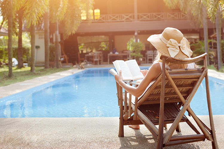 woman relaxing and reading a book by the pool of a home in Los Angeles